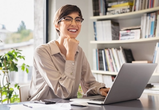 Mujer sentada con una computadora portátil sonriendo en una oficina en su casa